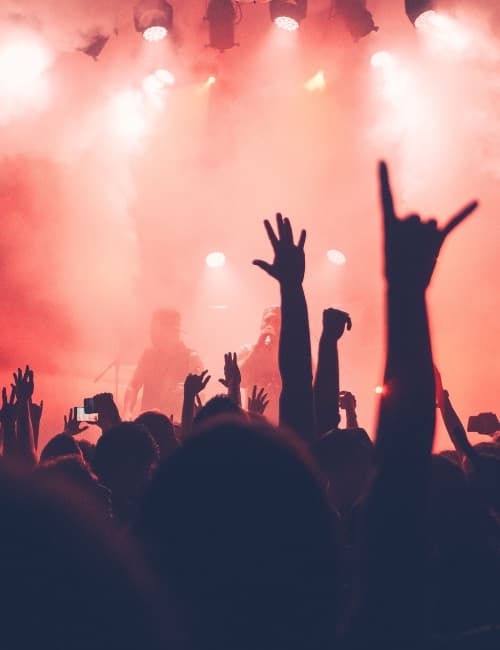 Hands raised in a festival crowd under red stage lighting